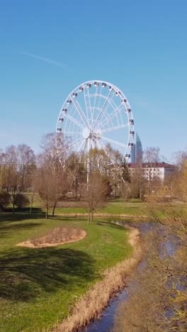 ferris wheel near river in riga with blue sky and distant business buildings