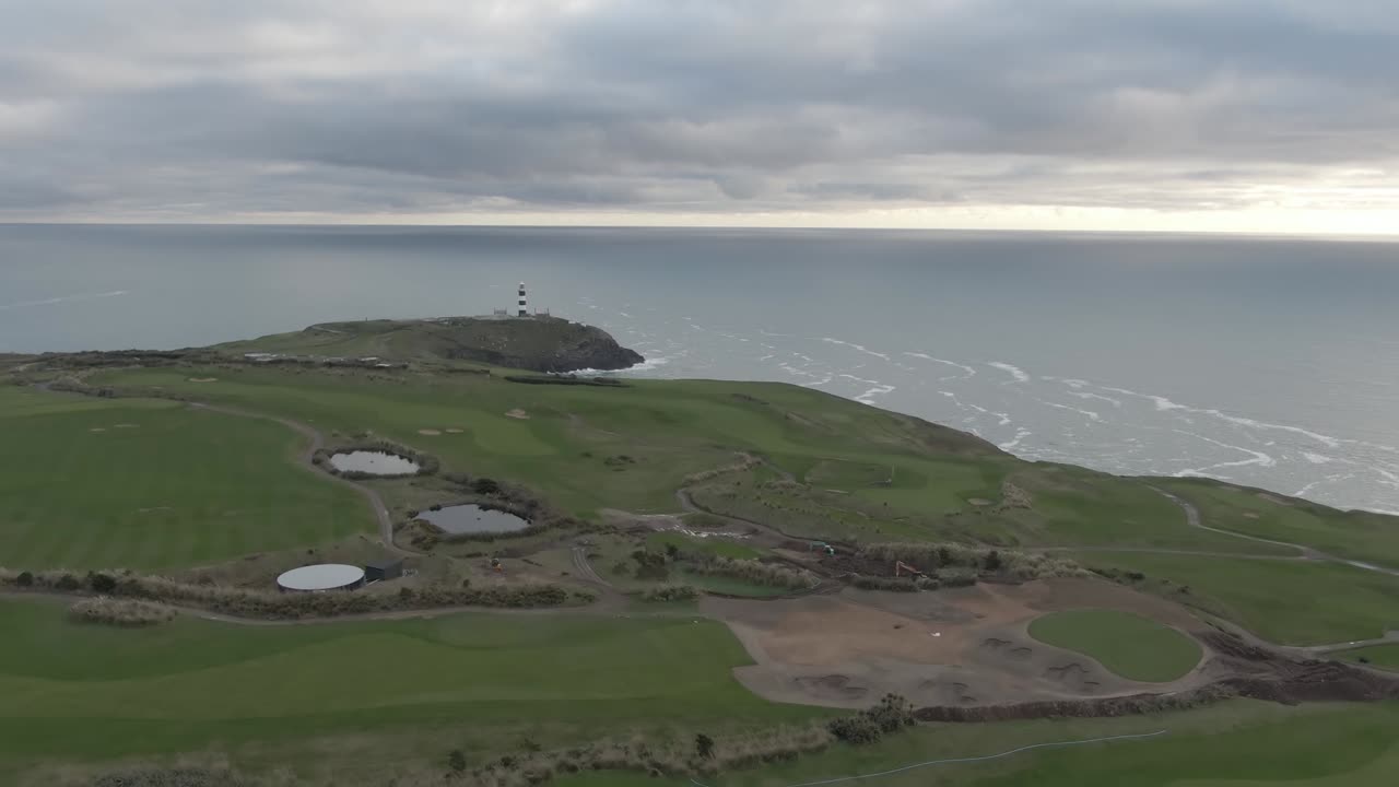 Aerial flight over irish golf course towards costal shoreline and approaching lighthouse in the pinninsula