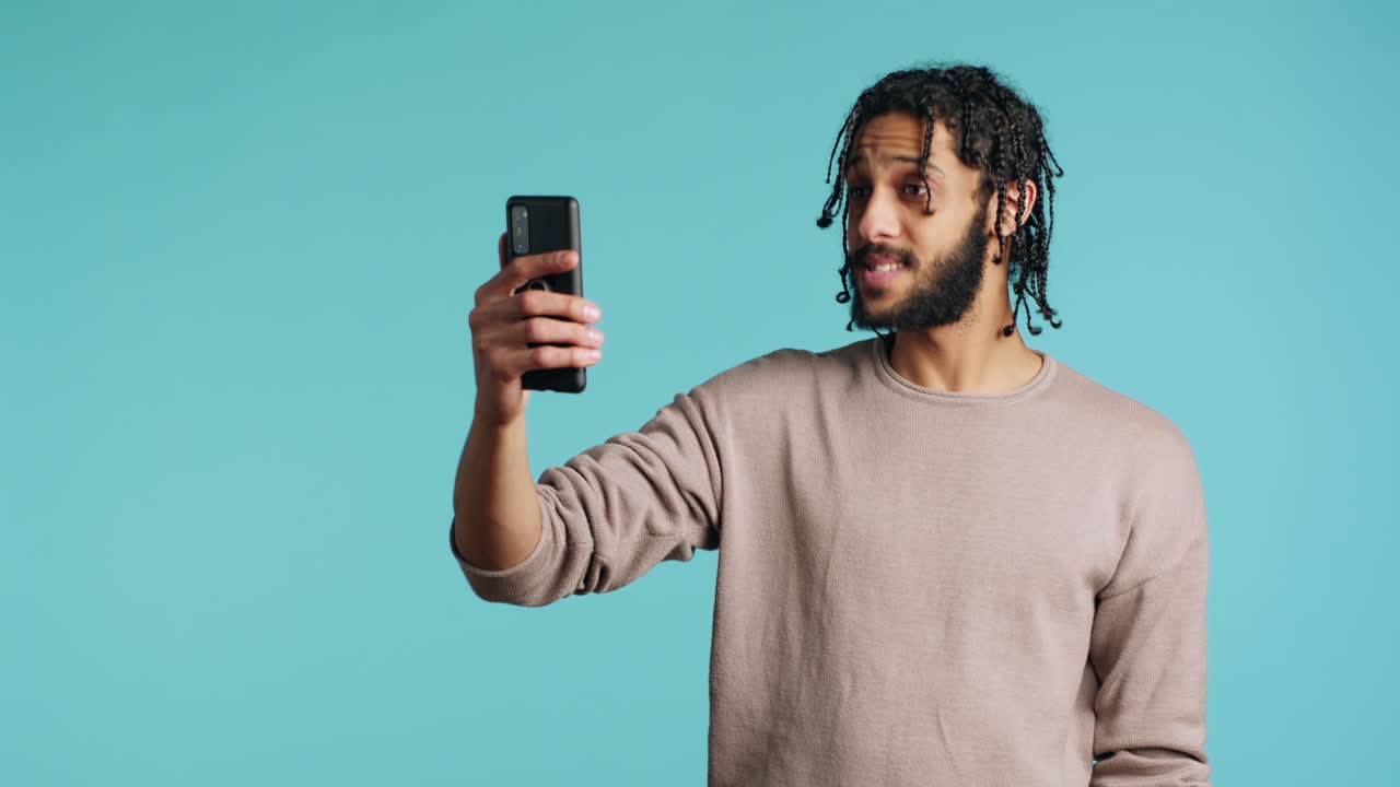 Man chatting with friend over online videocall on smartphone, studio background