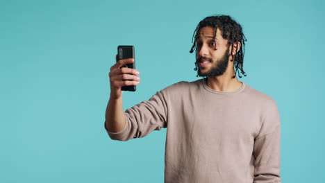 Man-chatting-with-friend-over-online-videocall-on-smartphone,-studio-background