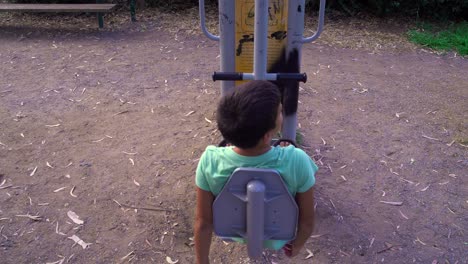 back view, high angle of 8 years old caucasian greek boy, exercising outdoors, at open public gym equipment, park of kalamata, greece 4k