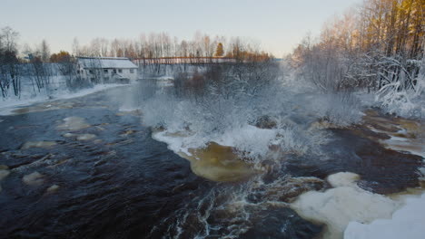 Vista-Estática-Del-Río-Por-Paisaje-Nevado-Y-Casa-Distante-En-Finlandia