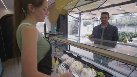 a happy customer receives a sample of ice cream from a smiling employee at an ice cream parlor with modern decor and a relaxed outdoor atmosphere.