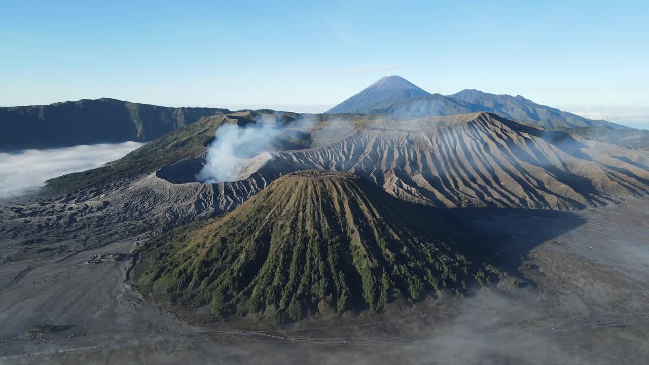 Beautiful cinematic drone shot of Bromo caldera, volcanoes, and Semeru mountain peak rising in the distance