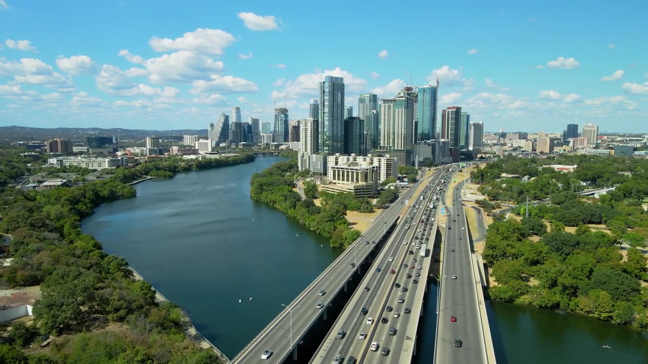 Voo de drone aéreo sobre Austin, Texas, mostrando o Rio Colorado, a Rodovia I35 e o centro da cidade ao fundo, durante o dia. Paisagem urbana americana.
