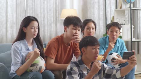 asian teenagers cheering and watching football game on smart phone and disappointed at home