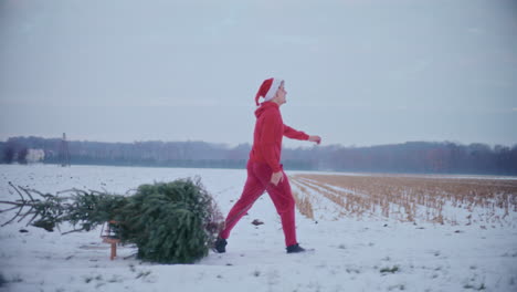 Smiling-man-pulling-sled-with-Christmas-tree-on-snow-covered-landscape