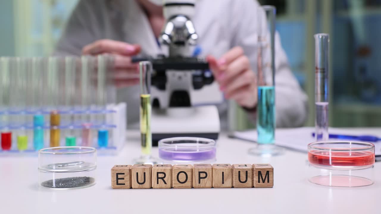 Kubus kayu mengeja kata europium di dekat peralatan gelas lab yang cerah.