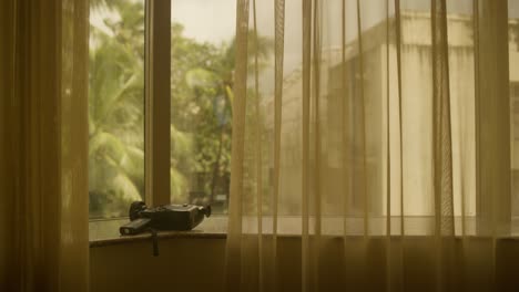 Canon-Super-8mm-Camera-on-Window-Sill-warm-room,-golden-heat,-india,-palm-trees-in-background,-warm-sheers-and-curtains-camera-photography-and-travel-video-capturing-memories-on-holiday