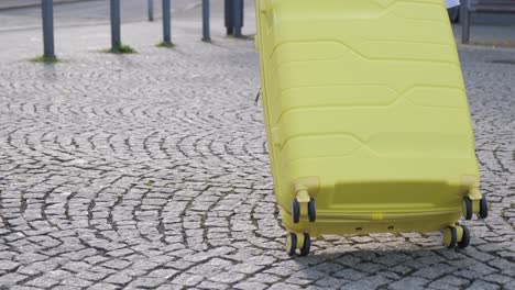 slow motion of a female tourist in a fashionable outfit walking down a european street and carrying her bright yellow wheeled suitcase. vacation and travel