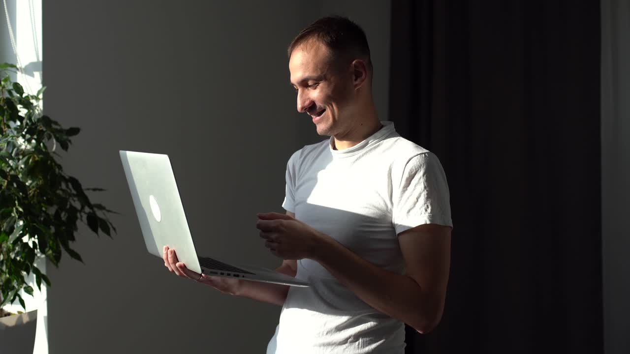 joven guapo trabajando con su computadora portátil y sonriendo mientras está de pie contra un fondo blanco.