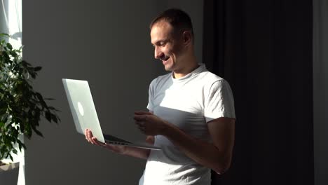 joven guapo trabajando con su computadora portátil y sonriendo mientras está de pie contra un fondo blanco.