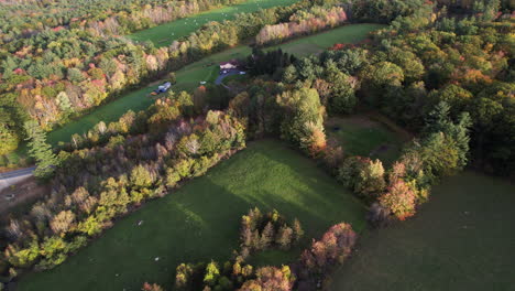 Aerial-view-of-New-Hampshire-countryside-ranch-on-sunny-autumn-day,-green-meadow-and-colorful-forest-foliage,-drone-shot