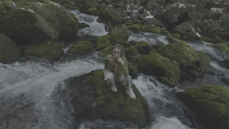 woman sits by a waterfall in a mossy forest