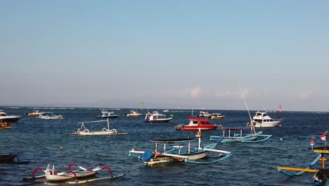 Toma-En-Cámara-Lenta-De-Barcos-Y-Barcos-Atracados-En-La-Bandera-Indonesia-De-Sanur-Beach-Bali-Ondeando-En-Un-Horizonte-Azul-Claro,-Sanur-Denpasar