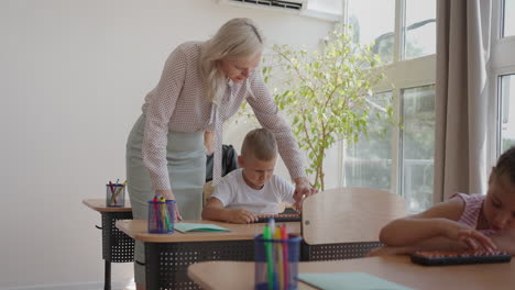 en la clase de escuela primaria: el profesor entusiasta camina entre filas de niños brillantes y diversos explica la lección. grupo de niños inteligentes multiétnicos aprendiendo cosas nuevas. vista lateral disparo de seguimiento