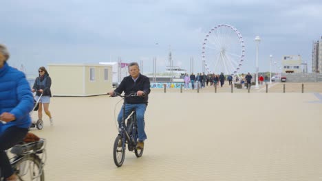 people walking on sea promenade near the beach of nieuwpoort with ferris wheel in background. holiday town by the belgian sea - slow motion