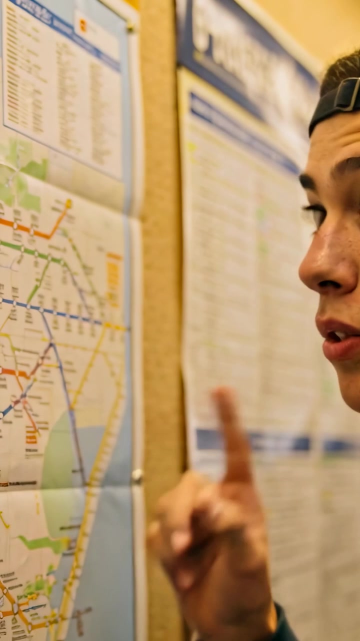 Vertical video: Needing route teen with cap pointing tracing map and times at station, copy space