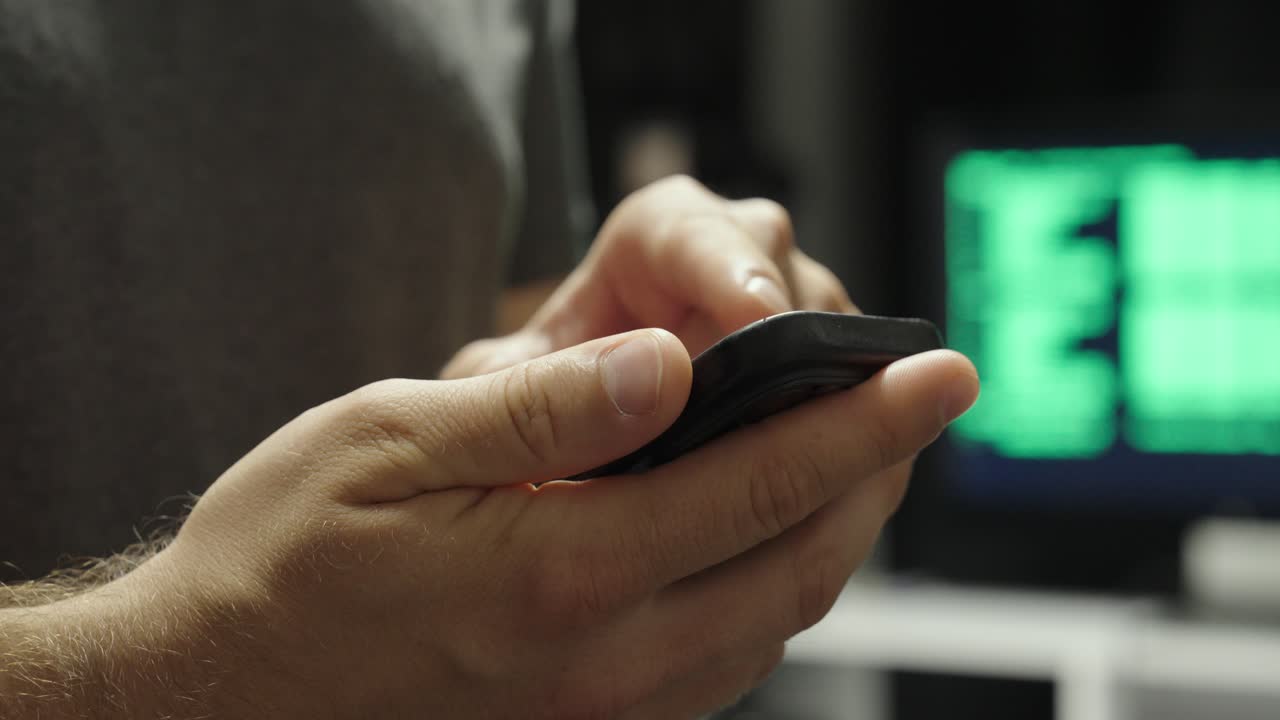 Close-up of a hand holding a smartphone using AI, with a display in the background showing AI code