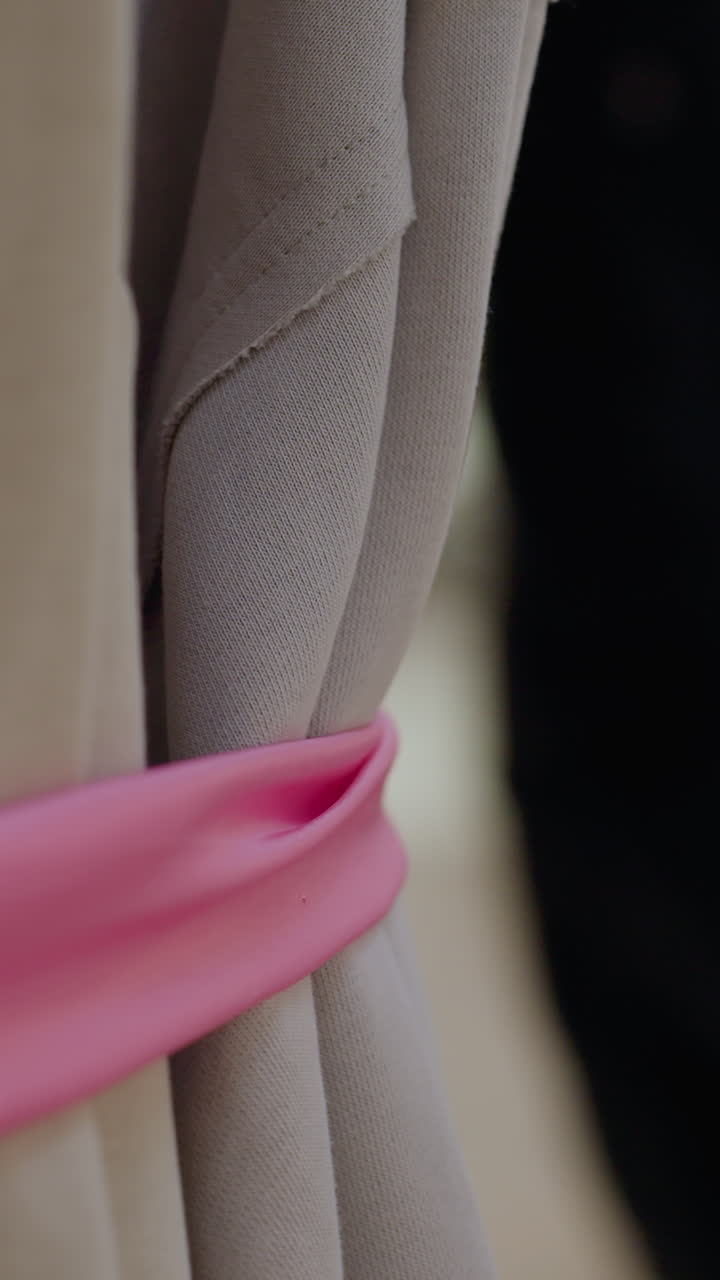 Close-up of hand holding fabric with blurred background showing people passing by in well-lit store, captures intimate shopping moment as customer examines clothing with others nearby