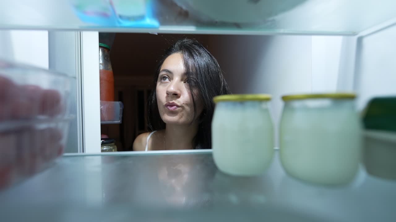 una mujer hambrienta abre el refrigerador y elige un bocadillo saludable dentro del refrigerador.