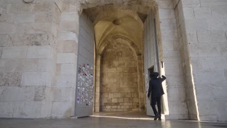 follow up shot of a model wearing black suit and hat entering a castle in jerusalem