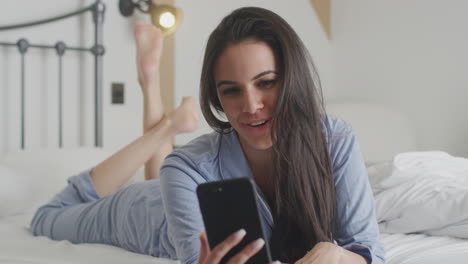 woman with mobile phone wearing pyjamas having video chat lying on bed