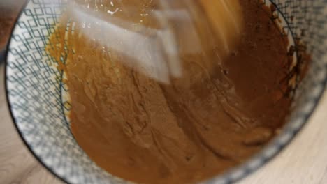 woman vigorously mixing dalgona coffee ingredients with hand whisk, closeup