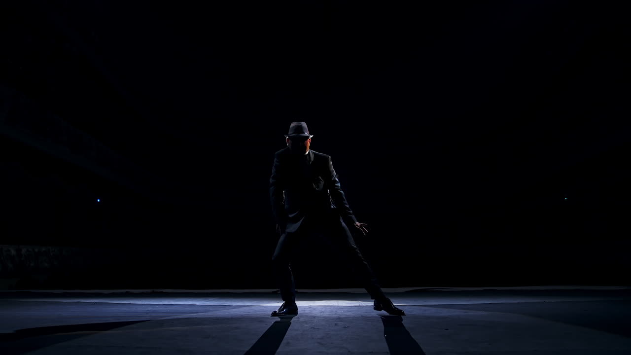 Senior man in costume on stage in darkness. Active man in hat dancing on stage during the performance in the theater.