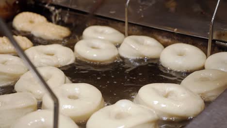 a cinematic close up of a bakers stick flipping a batch of fresh doughnuts in a homemade oil-filled fryer