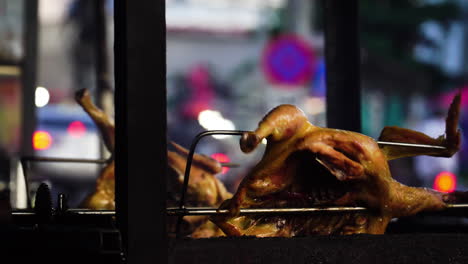 Asado-De-Pato-Vietnamita-En-Parrilla-Giratoria,-Tráfico-De-La-Ciudad-En-Segundo-Plano