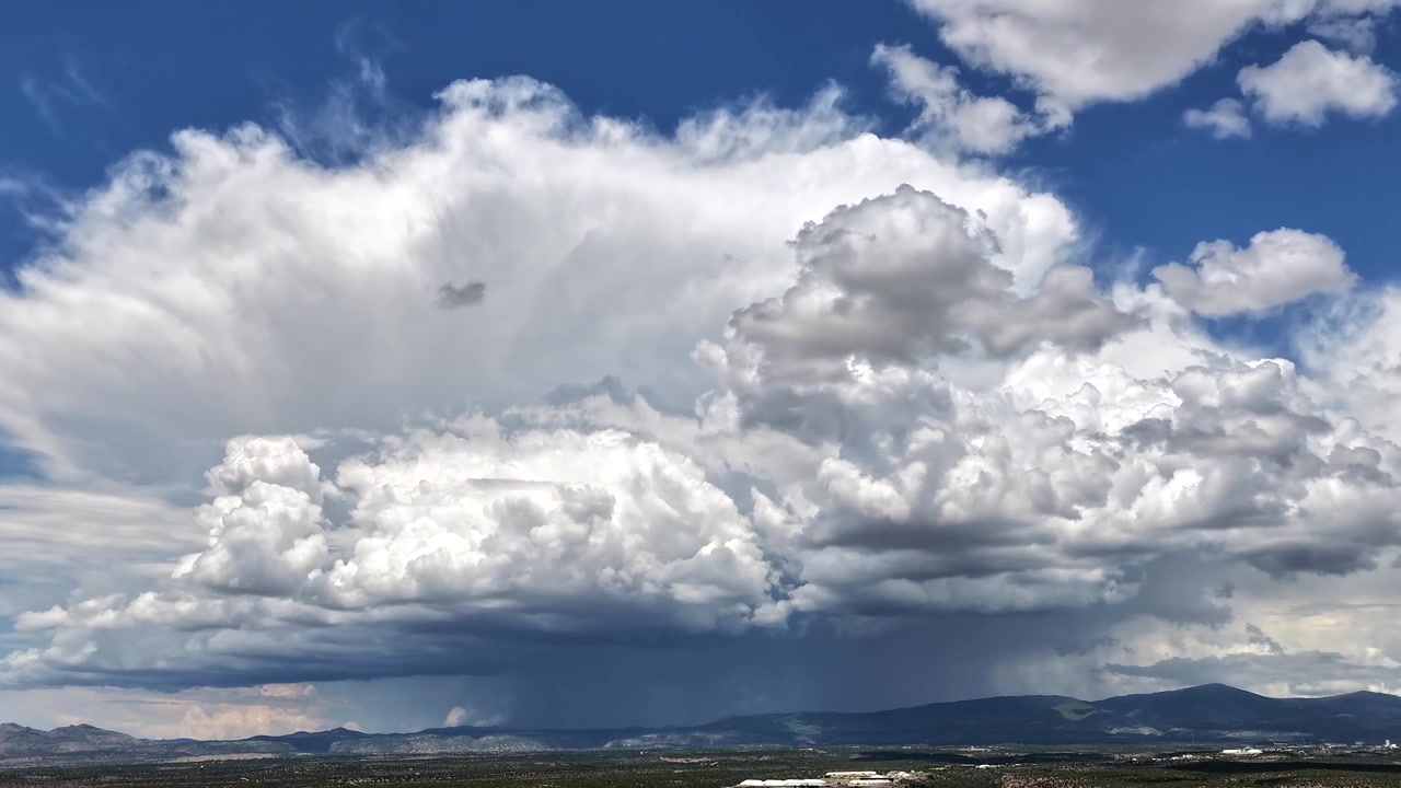 Timelapse 4K con drone di un gigantesco sistema temporalesco monsonico su un paesaggio desertico d'alta quota. Nuvole cumulonembi in rapido movimento si gonfiano mentre pesanti scrosci di pioggia cadono sull'orizzonte montuoso distante.