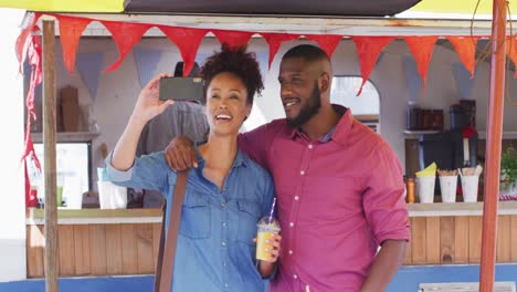 pareja afroamericana sosteniendo batidos sonriendo mientras se toman una selfie en el camión de comida