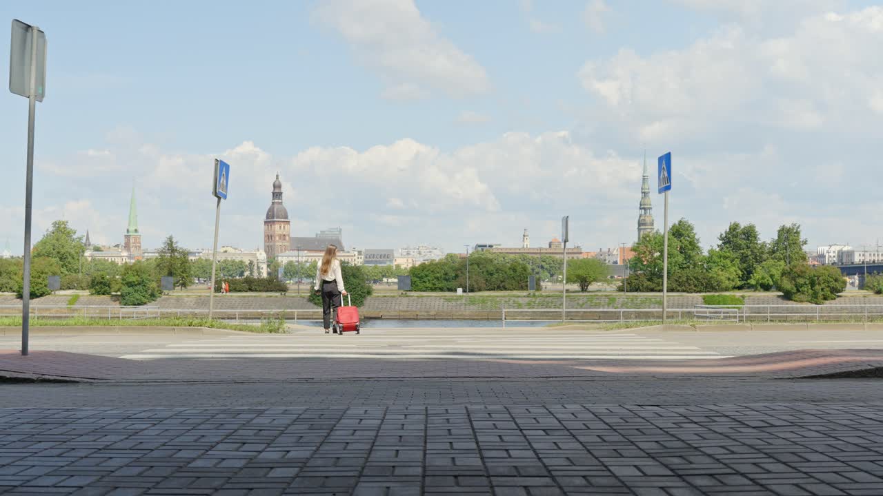 Неузнаваемая брюнетка с красным чемоданом в Риге в солнечный день