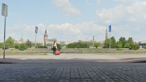 unrecognisable brunette woman with red suitcase in riga on sunny day