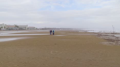 a long view of three tourists walking on the beach of barcelona, catalonia, spain