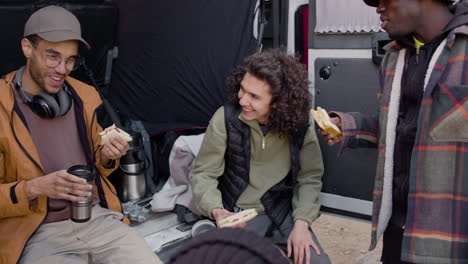 un equipo de producción de películas tomando un descanso mientras come un sándwich y habla detrás de una camioneta en la calle 1