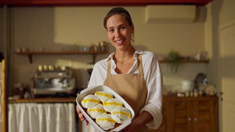 una panettiera sorridente in un caffè, che mostra dessert appena cotti