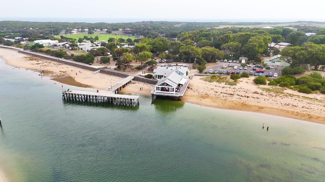 Aerial footage captures Barwon Heads pier and beach with serene waters and lush greenery under soft daylight