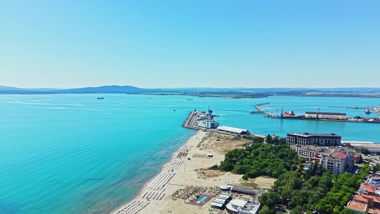 Giornata luminosa in spiaggia con cielo sereno e barche nel mare blu vicino al molo dove le persone si godono attività ricreative.