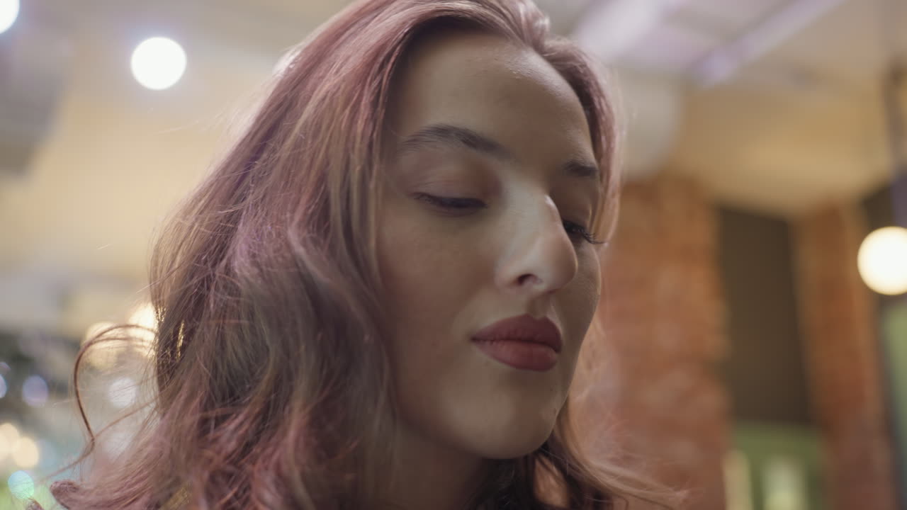 Close up of woman with curly hair and pointed nose looking upward with calm expression, set against warm softly lit interior, highlighting facial features and natural beauty in serene moment