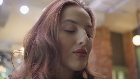 close up of woman with curly hair and pointed nose looking upward with calm expression, set against warm softly lit interior, highlighting facial features and natural beauty in serene moment