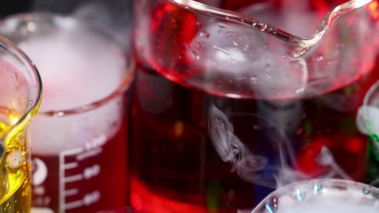 Close-up of beakers with red, yellow, and green liquids emitting vapor.