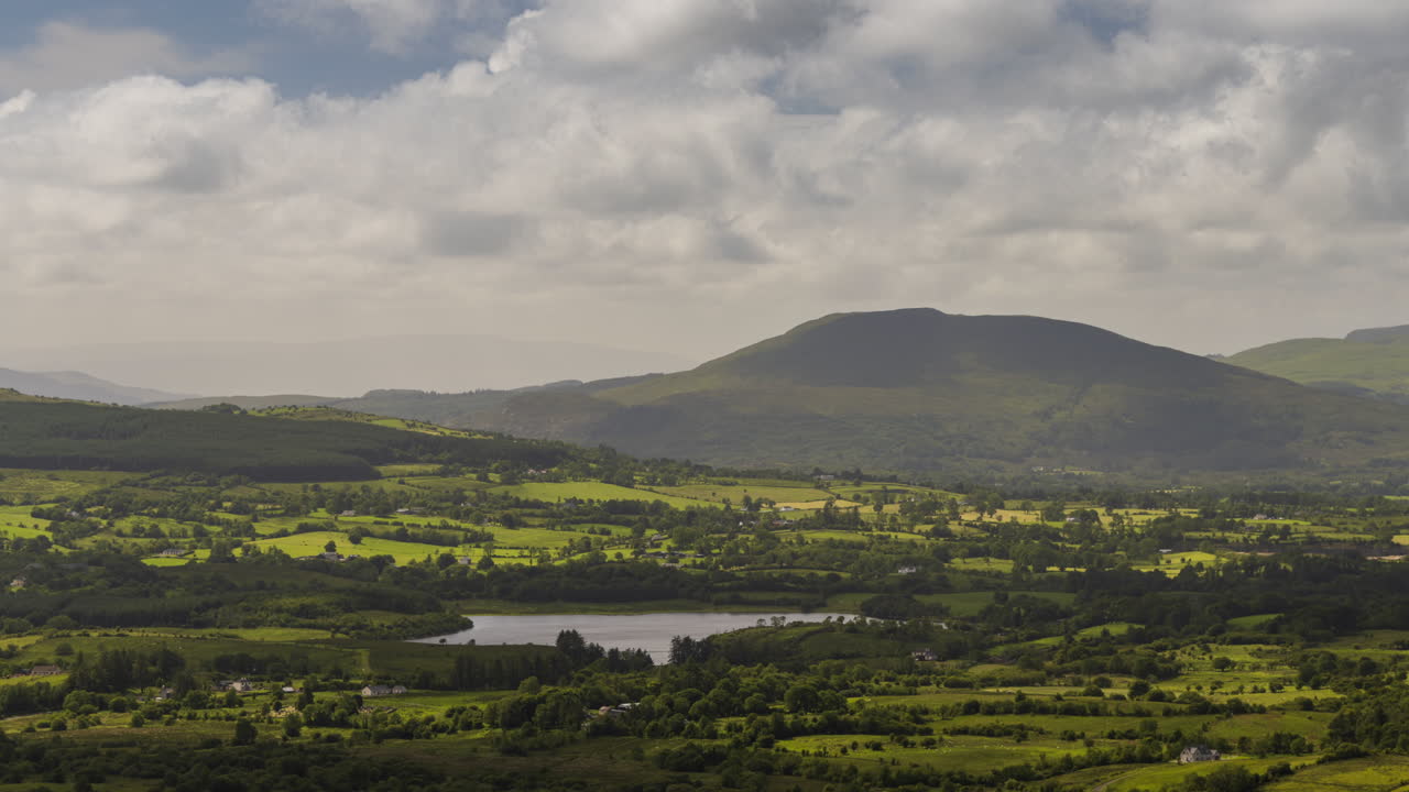 lapso de tiempo del paisaje verde de la agricultura rural con granjas, lagos y colinas en la distancia en un día nublado de verano en irlanda