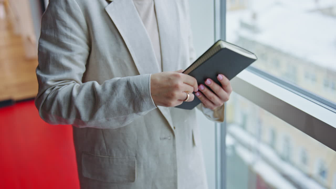 Woman in a light gray blazer looking out a window with a notebook