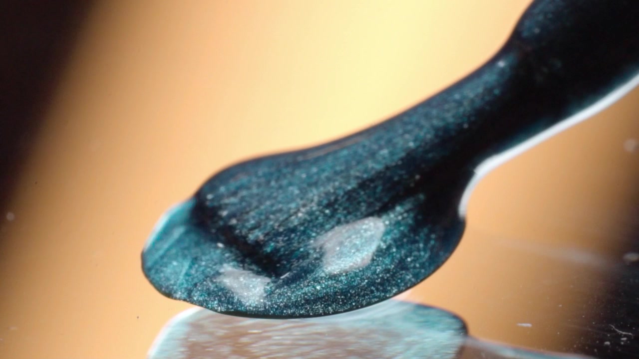 Macro primo piano di crema cosmetica metallica su spatola nera. Il prodotto di bellezza scintillante mostra una texture liscia e una finitura riflettente nei minimi dettagli