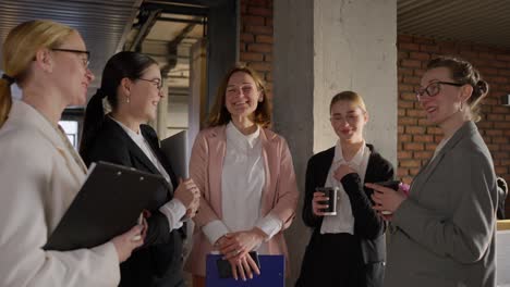 A-group-of-confident-business-girls-in-glasses-and-business-suits-stand-in-a-semicircle-and-chat-during-a-break-from-work-in-a-modern-office