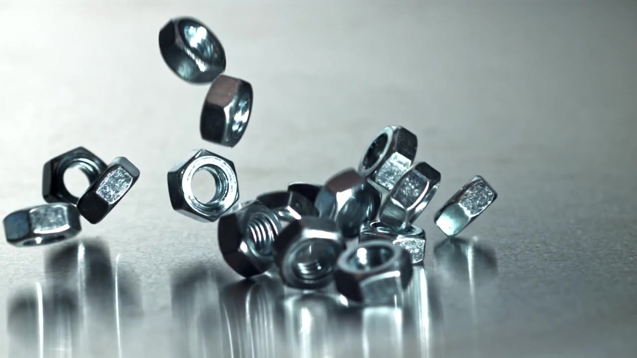 Nærbillede af metalmøtrikker, der falder i slowmotion ned på en reflekterende overflade