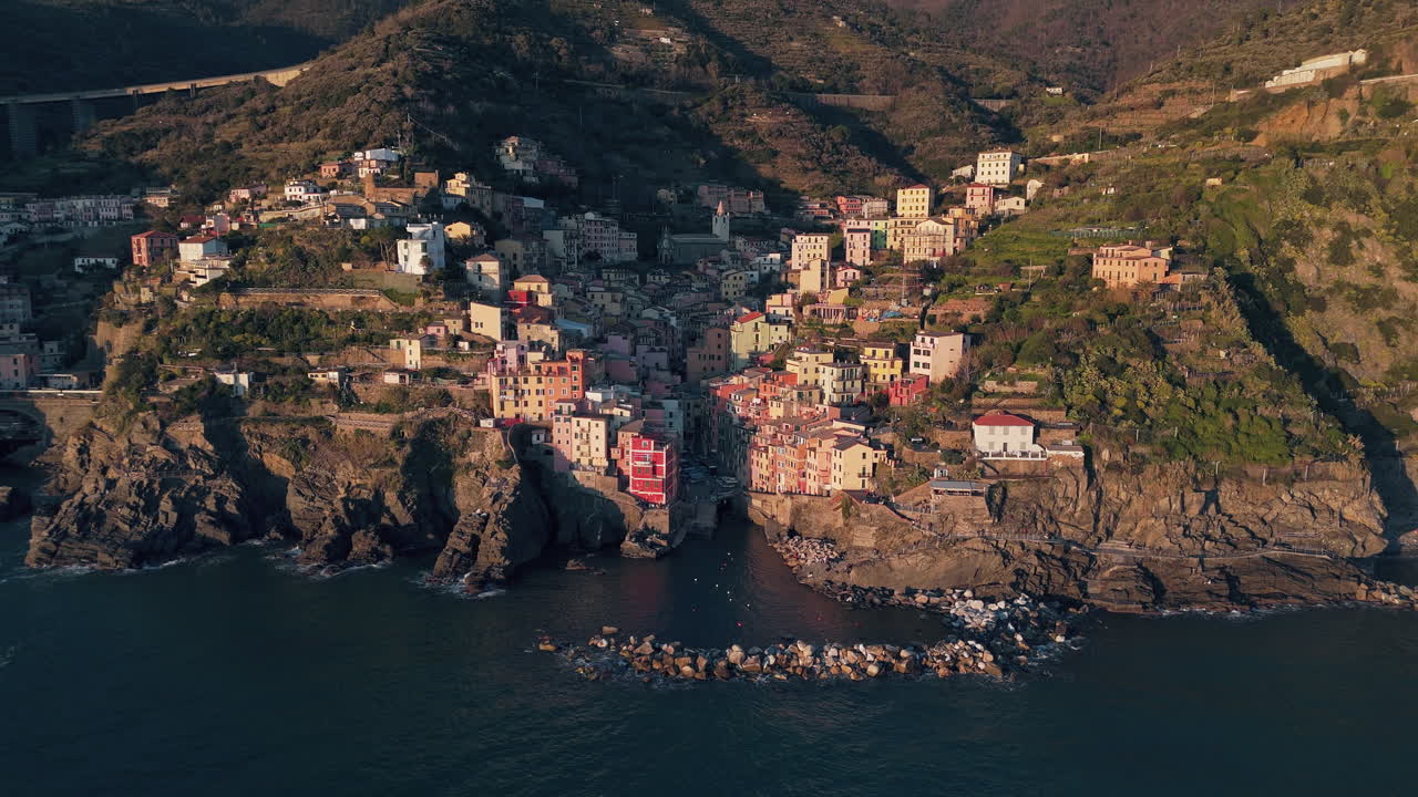 Edifici costieri colorati nel borgo di Riomaggiore con il sole che proietta una luce dorata.