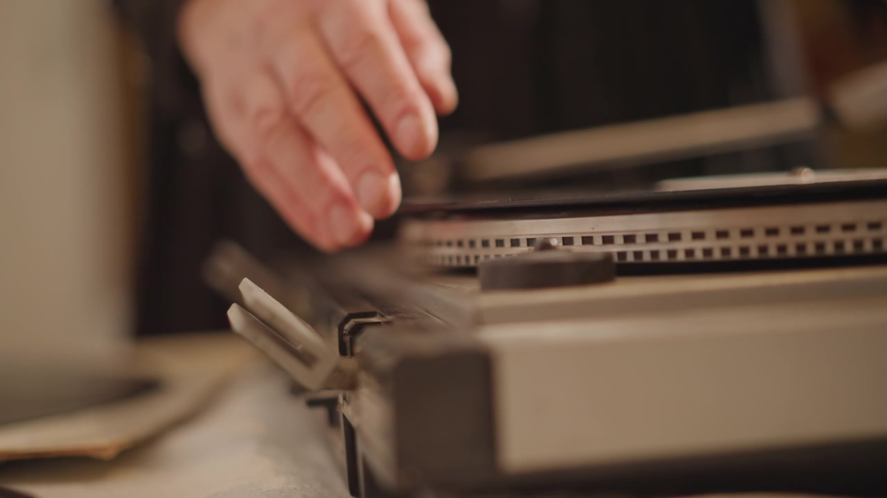 Nærbillede af hvide hænder, der kalibrerer tonearmen på en vintage pladespiller. Varmt lampeskær. En forsigtig tekniker justerer nål og pickup. Synlig pladetallerkenkant og etiket. Værktøj og papir på bordpladen. Lav dybdeskarphed.